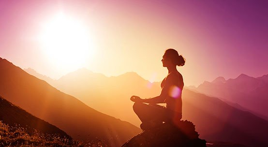 Kvinna mediterar på ett berg och visar psykologin bakom viljestyrka