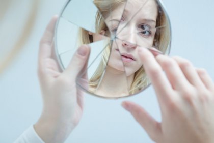 Kvinna ser sig själv i trasig spegel