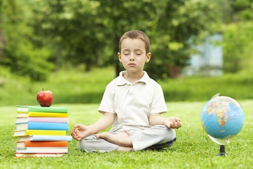 Pojke mediterar i gräset med skolböcker bredvid sig