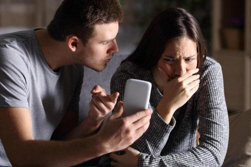 Aggressiv man pekar ilsket på en ledsen kvinnas mobiltelefon
