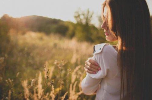 Kvinna i profil ute i soligt naturområde håller sig om axeln