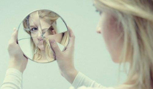 En kvinna tittar på sig själv i en trasig spegel