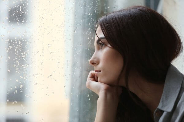 Nedstämd kvinna tittar ut genom regnigt fönster
