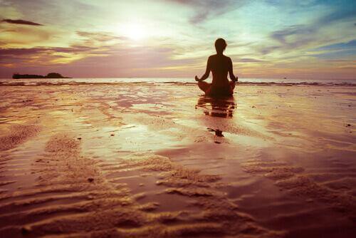 Kvinna som sitter vid havet och mediterar.