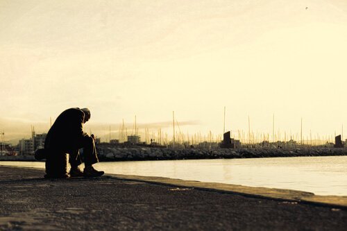 En sorgsen gammal man sitter själv framför en sjö.