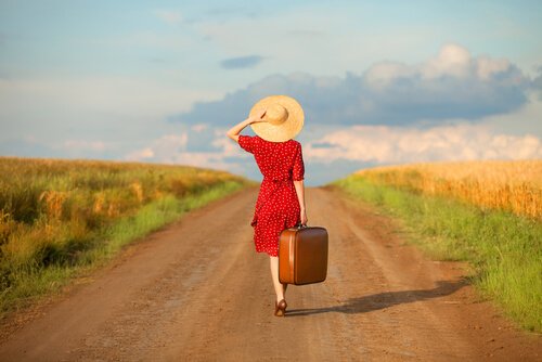 En kvinna med en resväska som går på en väg.