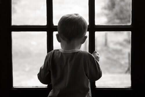 En liten ledsen pojke tittar ut genom fönstret.