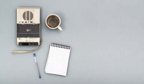 En inspelare bredvid en kopp kaffe, ett skrivblock och en penna.