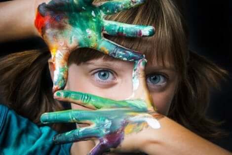 En liten flicka med målade händer som inramar hennes öga