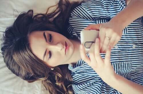 En kvinna som ligger på sin säng och tittar på sin mobiltelefon