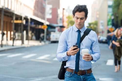 En man som går på gatan och tittar på sin mobiltelefon