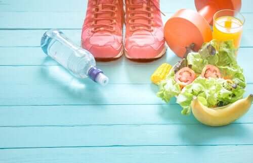 Hälsosam mat, tennisskor, en hantel och en flaska vatten på ett blått golv