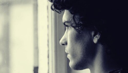 Ung man ser ut genom fönster, ensam