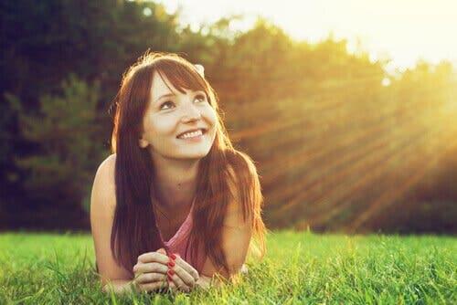 En leende tjej ligger i gräset och tänker på relationen mellan optimism och hälsa