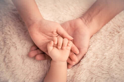 En barnhand ovanpå händerna på en vuxen för att undvika anaklitisk depression