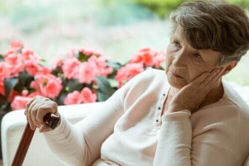 En äldre dam sitter på en soffa framför blommor