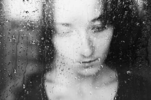 En ledsen kvinna som ser ut genom ett regnigt fönster