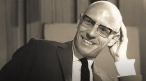 En svartvit bild av Michel Foucault: han ler