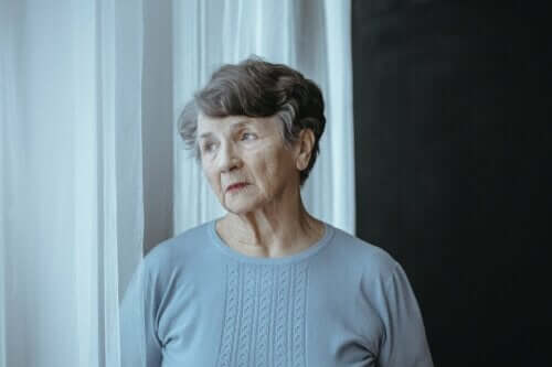 En äldre dam står och tänker vid ett fönster