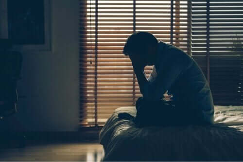 En nödställd man sitter ensam i en säng, i ett mörkt rum, med huvudet i händerna