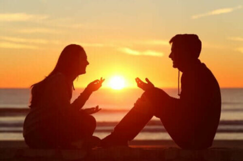 Två personer sitter vid havet och pratar med solnedgången som bakgrund