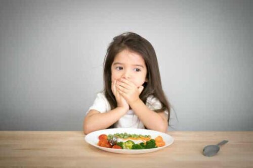 En flicka täcker munnen framför en tallrik med grönsaker