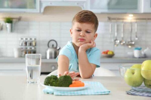 En pojke skjuter undan en tallrik med broccoli och morötter